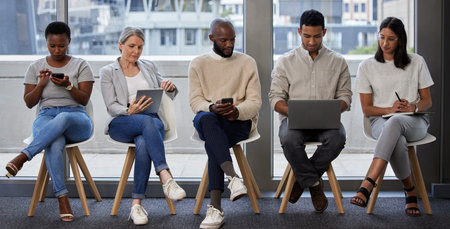 Business people, row and waiting room with technology for interview, career news or job opportunity at office. Young group of employees in line with laptop, tablet or phone for research or networkingの写真素材