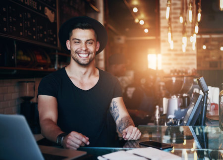 Portrait, coffee shop and man in cafe with laptop for small business, working online and customer service. Restaurant, hospitality and waiter by counter with computer for serving, help and inventoryの写真素材