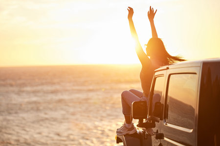 Sunset, car and happy woman with freedom by the sea with road trip adventure and journey by the...