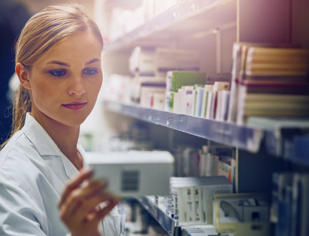 Pharmacy, shelf and woman with box of drugs, pills or search for prescription medicine inventory. Pharmacist, reading and working in shop with sale of medical product for healing or healthcareの写真素材