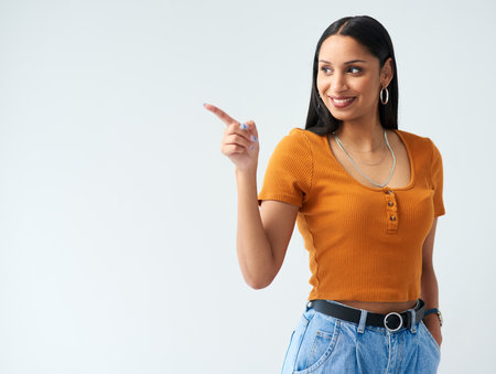 Happy, pointing and hispanic woman in studio for news, deal or coming soon announcement with white background. Smile, mockup and female person with hand gesture for promotion, advertising or discountの写真素材