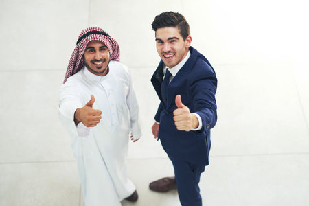 Arab, business and people with thumbs up in office, agreement and company opportunity approval for deal. Employee, diversity and trust or support, collaboration and professional with hand gestureの写真素材