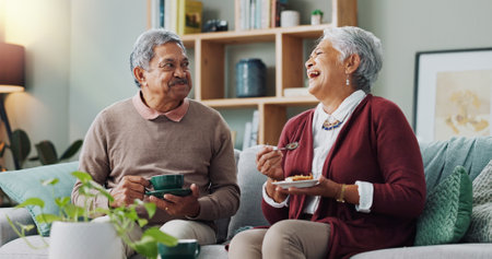 Senior couple, happy and coffee on sofa in house, home and living room for retirement. People, elderly partners and family drinking tea, cake and food for laugh or relax on couch for love and bondingの写真素材