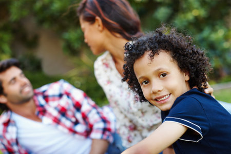 Portrait, boy and family together in park, son and happy with relax mom and dad in nature for relationship bonding. Growth, childhood development and vacation or holiday outside, love and caringの写真素材