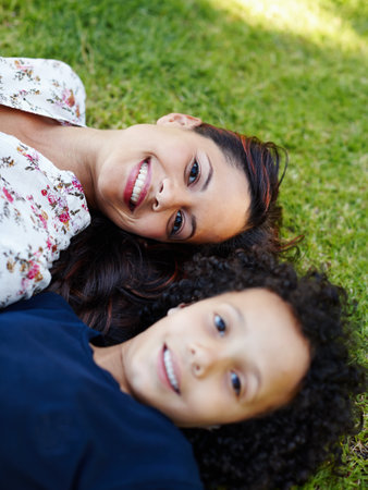 Face, mom and child lying on grass in garden to relax in summer, vacation or picnic in holiday. Family, happiness and portrait of mother with kid on lawn in backyard and smile together from aboveの写真素材