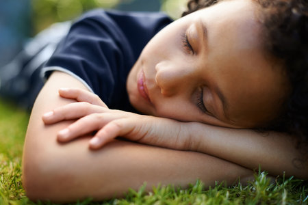 Boy, kid and sleeping on grass in garden of home for resting, exhausted and tired with dreaming in nature. Child, fatigue and nap on lawn in backyard with comfort, peace or relax for wellness outdoorの写真素材