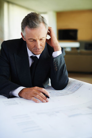 Stress, blueprint and mature man in office, thinking and planning for risk of investment in property. Real estate, realtor and executive of business, reading and anxiety of paperwork for budgetの写真素材