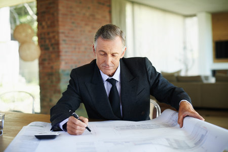 Suit, blueprint and mature man in office, finance and calculator for tax of investment in property. Real estate, realtor and executive of business with floor plan and paperwork for budget on deskの写真素材