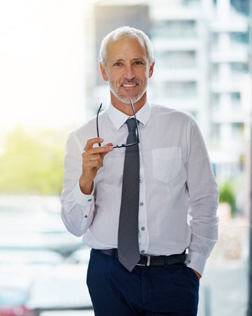 Portrait, executive and man with smile in office, glasses and vision for employee and happiness in job. Corporate, boss and mature person in workplace, investment specialist and accountant in companyの写真素材