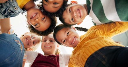 Huddle, support and happy children in school for education, community or development. Low angle, diversity and group of friends with smile in playground for solidarity, teamwork or playing togetherの写真素材