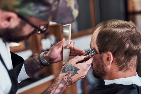 Hair care, customer and man in barbershop with machine, cut and tools for trendy hairstyle trim at small business. Style, barber and client in chair for grooming service, haircut skills and shaveの写真素材
