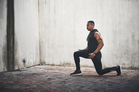 Man, fitness and lunge with earphones in city for strong muscle, balance and exercise for wellness. African person, music and workout for legs with listening, health or audio streaming in New Yorkの写真素材