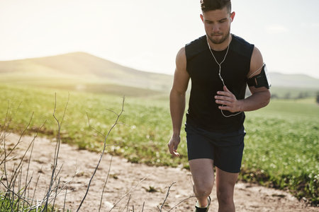 Man, earphones and music for running in outdoor, marathon training and health in countryside. Male...