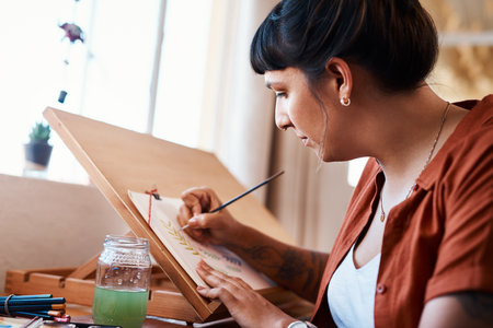 Watercolor, painting and artist with easel in home and creative inspiration on canvas with project. Painter, working and woman sketch with brush on paper in workshop with talent and skill in artの写真素材