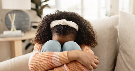 Sad girl, crying and sofa with stress in anxiety, loneliness or abuse in living room at home. Little female person, lonely child or kid alone on lounge couch with emotion, fear or grief in depressionの写真素材