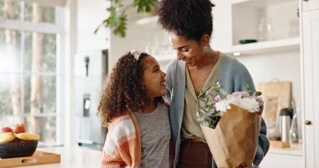 Kitchen, mother and girl with smile, flowers and present for mothers day, love and family in house. Home, mom and daughter with embrace, happiness and cute in apartment, woman or child with giftの写真素材