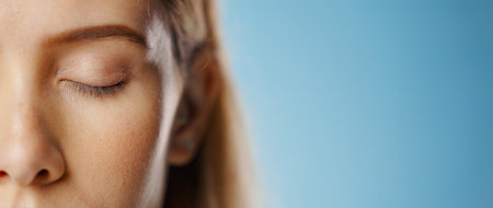 Eyeshadow, makeup and face of woman in studio for beauty, cosmetics or glamour on blue background. Closeup, banner and model with eyes closed for foundation, glowing skin or aesthetic transformationの写真素材