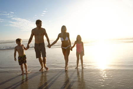 Sunset, love and family holding hands at a beach for summer, fun and bonding in nature together. Travel, people and children with parents at sea for vacation, journey or tropical adventure in Floridaの写真素材