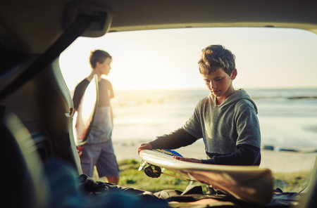 Beach, summer and boys at car with surfboard for holiday, outdoor adventure and fun weekend together. Travel, surfing and brothers in vehicle at ocean for water sports, waves and bonding at sunsetの写真素材
