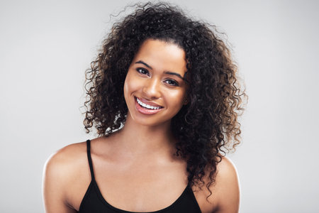 Confident, woman and portrait with hair care in studio for shampoo growth, treatment and shine. Happy, person and smile with pride for salon, natural texture and curly hairstyle on white backgroundの写真素材