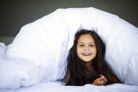 Home, happy and little girl in portrait in bed for relaxing, resting and comfortable with smile. House, bedroom and child under cover, duvet and adorable kid lying with innocent face in morningの写真素材