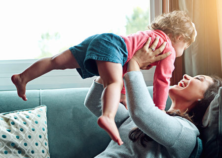 Playing, mother and child flying on sofa in living room together for bonding, connection and...