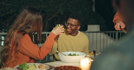 Friends, toast and outdoor dinner on patio, night and conversation with food, new years eve and party. Women, man and group at table with juice, memory or celebration with cheers, diversity and eventの写真素材