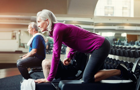 Mature woman, bench and weightlifting with dumbbell for workout, training or indoor exercise at gym....