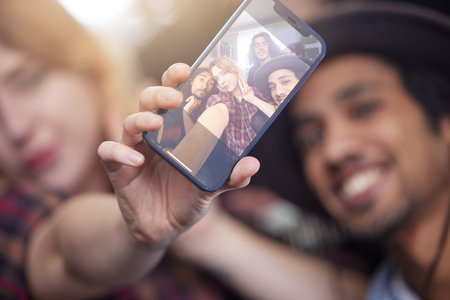 Hand, phone screen and selfie with friends in band for memory, profile picture or social media post. Art, backstage and photograph with group of young people together for gig, performance or practiceの写真素材