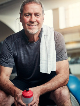 Relax, gym and portrait of mature man with smile, fitness and happiness with water bottle at workout. Exercise, training and confident athlete on break with pride, health and wellness in sports club.の写真素材