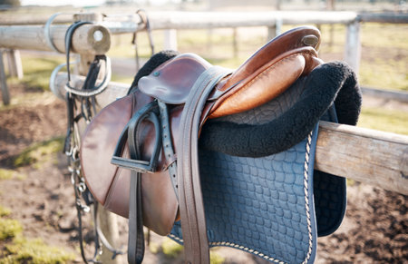 Saddle, countryside and farm on stable fence for riding or equestrian sports in nature or park. Background, agriculture or field in Texas ranch with seat or equipment for outdoor hobby in paddockの写真素材