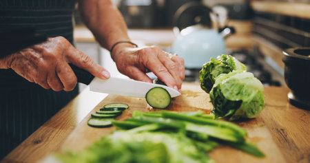 Hands, cutting board and salad in kitchen with green vegetables for healthy food or nutrition. Person with culinary skills for cooking lunch with lettuce, cucumber and organic ingredients at homeの写真素材