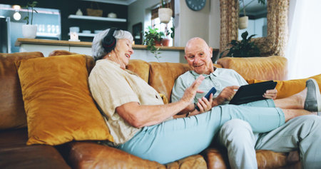 Senior couple, phone and texting on couch with tablet, choice or click for video, download or search in home. Elderly woman, man and smartphone on lounge sofa with discussion for chat on social mediaの写真素材