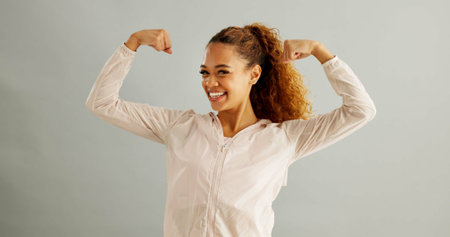 Happy, portrait and woman flex in studio for achievement, satisfaction or celebration on gray...