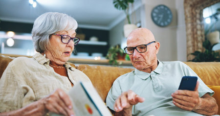 Senior couple, phone and reading with book on sofa for info, literature game or dictionary at home....