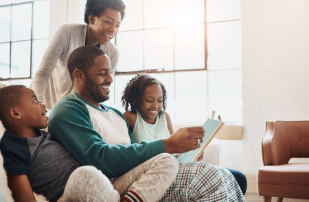 Reading, book and children with parents on sofa for bonding together on fathers day at home. Happy, knowledge and black family relaxing in living room with story or novel for language development.の写真素材