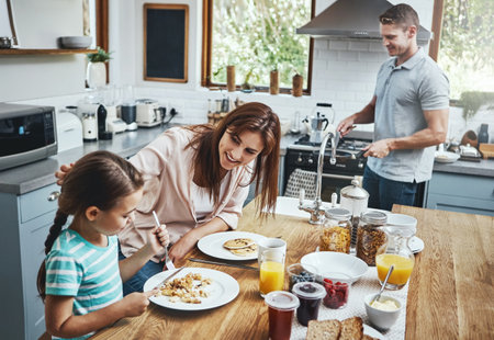 Love, breakfast pancakes and family bonding with children, mother and father, happy and prepare ingredients. Morning food, cooking and hungry woman, man and daughter in home kitchen eating mealの写真素材