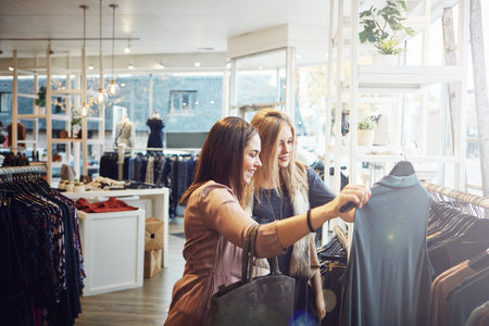 Smile, shopping and help customer with clothes for decision, sales or discount at luxury mall. Fashion, retail store or client with fabric at boutique for choice or advice with women talking at shopの写真素材