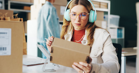 Industry, headphones and woman with package, box and parcel with ecommerce, delivery and entrepreneur. Business, sound and worker with cardboard, logistics order and listening to music with headsetの写真素材