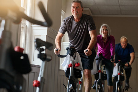 Spin class, senior or man on bike in workout or training for cycling progress, health or wellness. Gym, group challenge or confident elderly person on bicycle machine for fitness, exercise and cardioの写真素材
