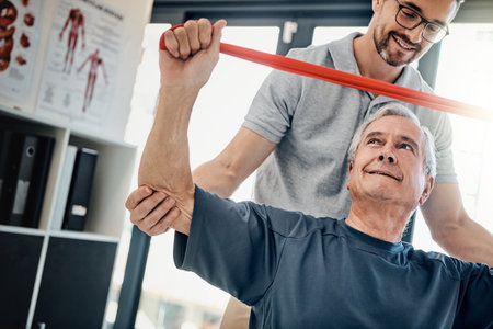 Clinic, physiotherapist and old man with resistance band, stretching and rehabilitation in healthcare. Physio, caregiver and elderly patient for mobility training, exercise and help in retirement.の写真素材