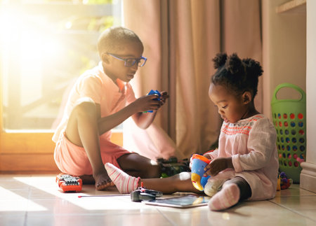 Black child, little girl and siblings playing with toys together on floor in living room at home. Young African, baby or toddler with playful brother for bonding, creativity or building help at houseの写真素材