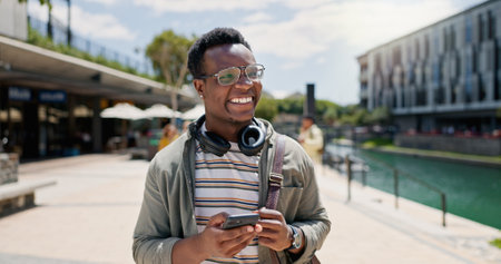 Education, laughing and phone with student black man on campus of college or university for learning. Development, funny and music with happy person outdoor at school for growth, scholarship or studyの写真素材