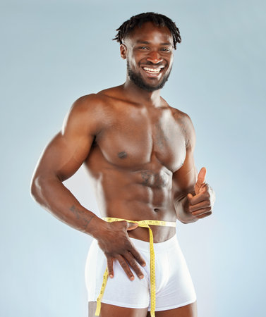 Weight loss, thumbs up and portrait of black man for fitness, workout and diet success in studio. Transformation, progress or results for exercise with tape and bodybuilder by white backgroundの写真素材