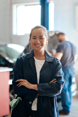 Portrait, mechanic or woman with arms crossed in garage, skills or service with small business. Face, equality or entrepreneur in auto repair shop, industry or opportunity with startup or fix vehicleの写真素材
