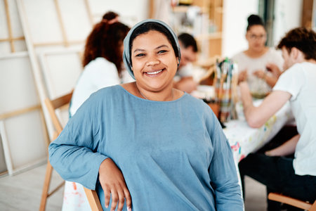 Portrait, Muslim woman and happy for paint and creativity in workshop with watercolor and friends. Artist, hijab and smile for painting in creative studio with canvas, acrylic and group art therapyの写真素材