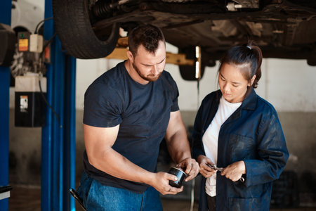 Mechanic, car and repair of fuel filter with services, solution or problem solving in engineering teamwork. People with part of vehicle or motor at auto shop, garage or workshop for maintenance checkの写真素材