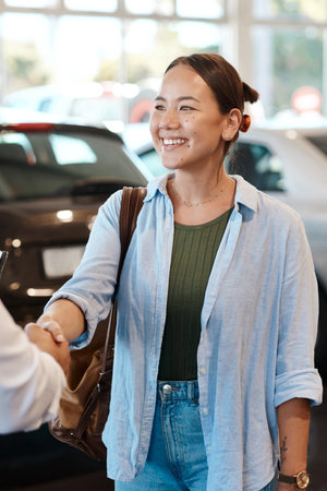 Car dealership, seller or happy woman shaking hands for vehicle, finance agreement or purchase. Payment, smile or customer in showroom for good service, transportation business or automobile loanの写真素材