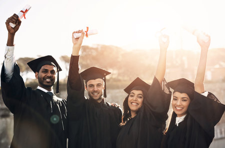 Students, graduation and happy with hands up on campus for celebration and success. People, college and university classmate or friends on smile on portrait for qualification, certificate and excitedの写真素材