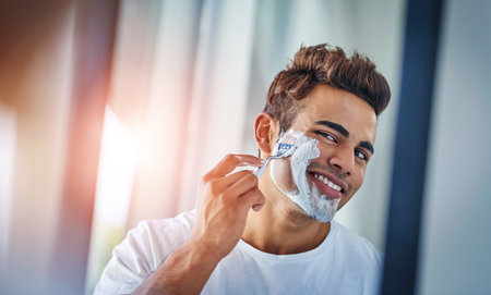 Home, mirror and man with shaving foam, dermatology and grooming routine for beard. Person, bathroom and guy with reflection, treatment and cream for self care, cosmetics and cleaning facial hairの写真素材